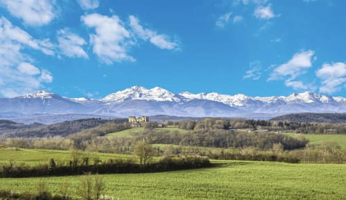 Snow-capped Pyrenees mountains overlooking green countryside and medieval castle near Mirepoix, Ariège