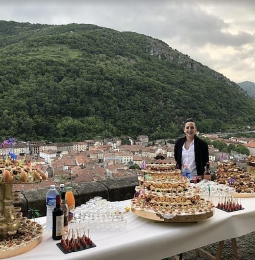 Mujer organizando un evento de vinos y aperitivos con vistas al pueblo de Mirepoix y las montañas, Ariège