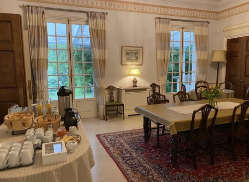 Élégante salle à manger du Domaine de Bize Mirepoix avec grandes fenêtres, table buffet ronde et sièges formels en Ariège