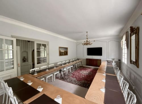 Salle de conférence moderne du Domaine de Bize Mirepoix avec tables en U, chaises blanches et moquette bordeaux en Ariège.