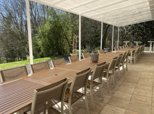 Longue table en bois avec chaises beiges sous une pergola blanche donnant sur les jardins du Domaine de Bize, Mirepoix