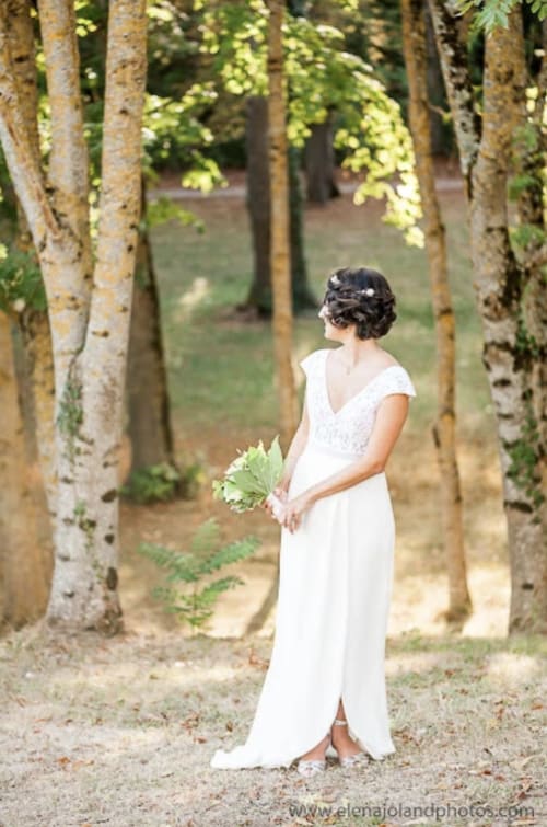 Braut im weißen Kleid mit Blumenstrauß auf der baumgesäumten Allee des Anwesens Bize Mirepoix in Ariège, Frankreich