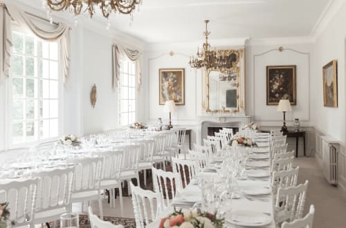 Élégante salle à manger du Domaine de Bize Mirepoix avec chaises blanches, verres en cristal et miroirs dorés ornementés.