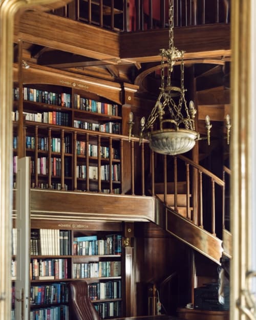 Multi-level wooden library interior with curved staircase, books, and ornate brass chandelier at Domaine de Bize Mirepoix