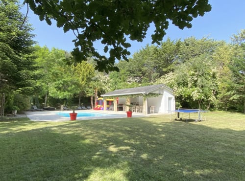Backyard with swimming pool, white cottage, trampoline, and lush trees at Domaine de Bize in Mirepoix