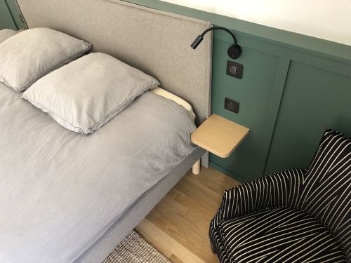 Chambre moderne à La Conciergerie Biarritz avec lit rembourré gris, oreillers blancs, table de nuit jaune et fauteuil rayé.