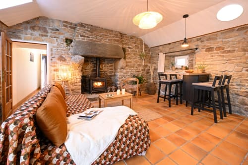 Spacious open-plan room at Espace Ker Gana in Plourin with stone walls, fireplace, leather sofa, dining area, and terracotta