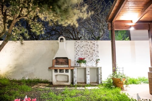 Area giardino esterna di Villa Il melograno a Bari con forno pizza vintage, muri bianchi, fiori in vaso e illuminazione della terrazza