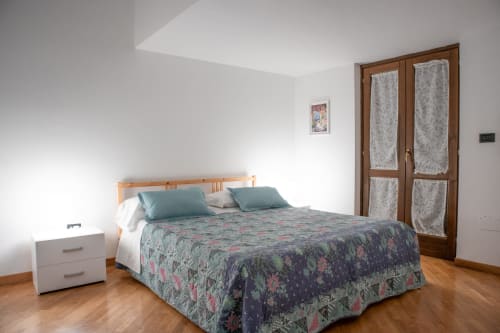 Camera da letto luminosa a Villa Il melograno a Bari con letto in legno, biancheria floreale, cuscini turchesi e giardino