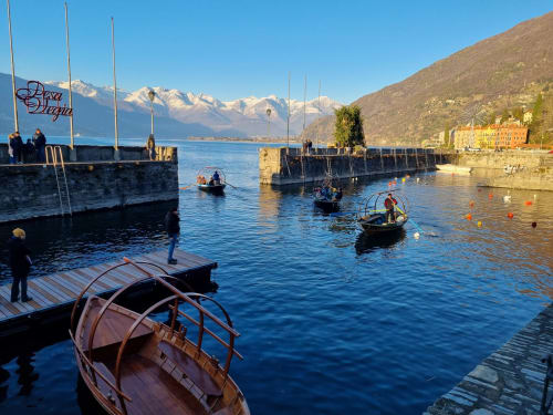 Traditional boats dock at Bellano harbor on Lake Como with snow-capped Alps and Villa Vista Lago di Como in background
