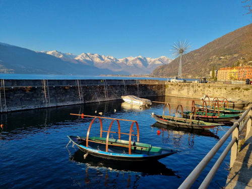 Colorful fishing boats moored in Lake Como with snow-capped Alps, Bellano waterfront and yellow buildings visible