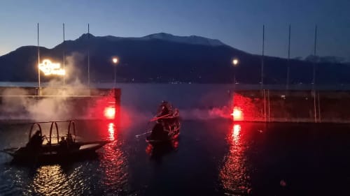 Red-lit boats on Lake Como at dusk with mountains and Villa Vista Lago venue lights, Bellano Italy