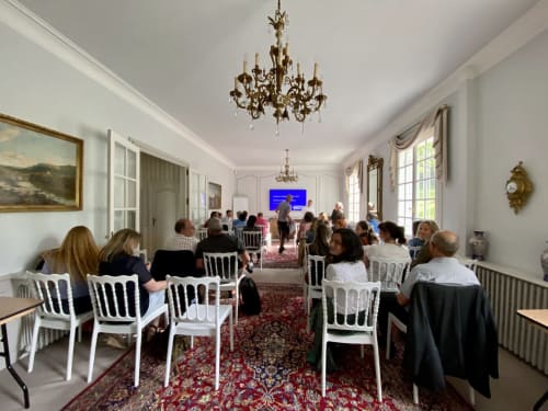 Élégante salle de séminaire du Domaine de Bize Mirepoix avec lustres, chaises blanches et participants écoutant une présentation