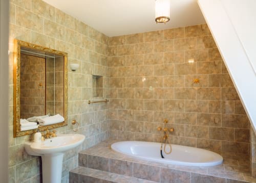 Salle de bains luxueuse avec murs en marbre, baignoire îlot, lavabo sur piédestal et accessoires dorés au Domaine de Bize à Mirepoix