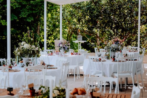 Eleganter Hochzeitsempfang im Freien auf dem Domaine de Bize Mirepoix mit weißen Tischen, Stühlen und Blumenarrangements