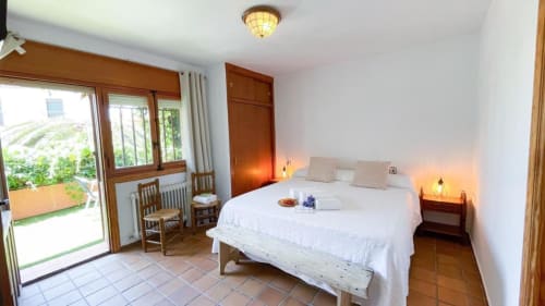 Dormitorio luminoso con ropa de cama blanca, muebles de madera, piso de terracota y puertas de cristal al jardín en Casa Rural Villa
