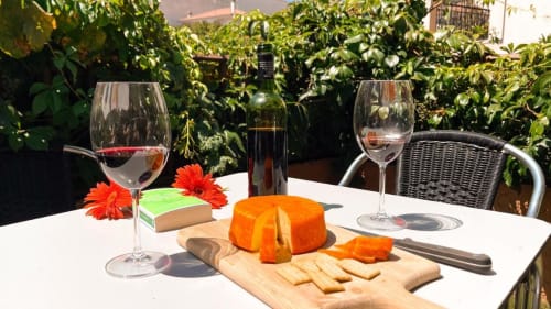 Comida al aire libre en el jardín de Casa Rural Villa del Jerte con vino, tabla de quesos y flores rojas en El Torno, Cáceres.
