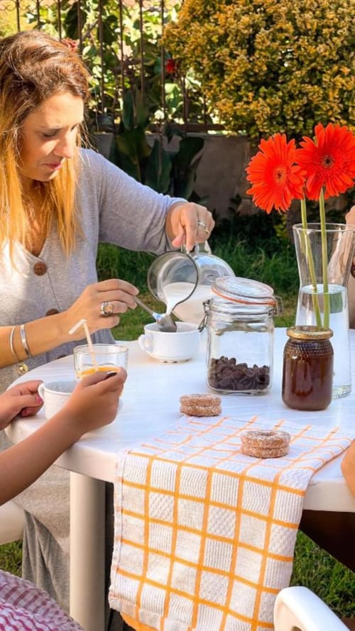 Mujer preparando refrescos en mesa al aire libre con flores rojas, en el jardín de Casa Rural Villa del Jerte