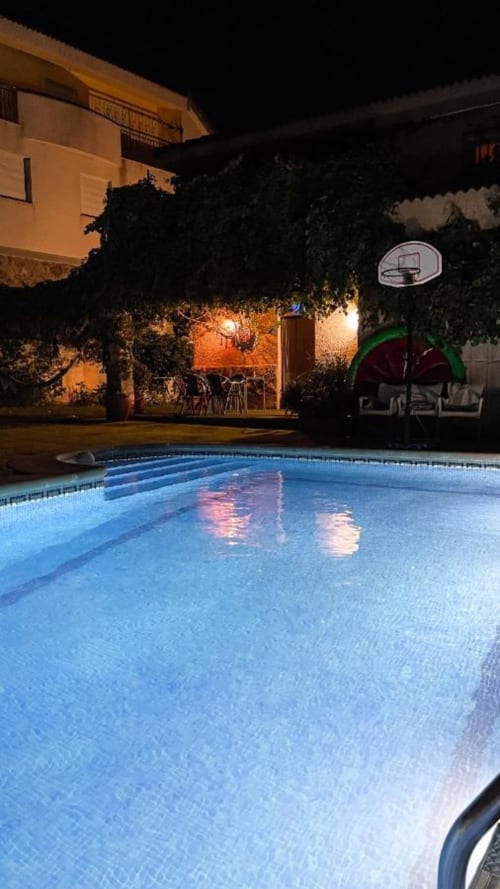 Illuminated swimming pool at Casa Rural Villa del Jerte in El Torno, Caceres, with lit courtyard and basketball hoop at night