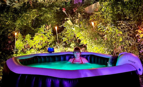 Guest relaxing in illuminated outdoor hot tub surrounded by lush garden at Casa Rural Villa del Jerte