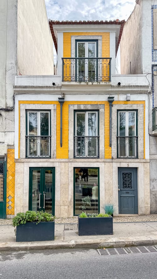 Fachada do hotel VAGO Alcântara Suites em Lisboa com janelas revestidas de azulejos amarelos, varandas ornamentadas e arquitetura portuguesa tradicional