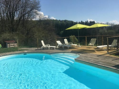 Espace piscine du Gîtes Des Planchettes à Marigny avec piscine bleue courbe, terrasse en bois, parasols, transats et cadre boisé