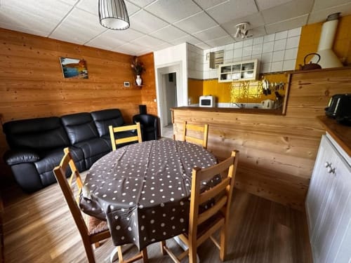 Intérieur chaleureux du gîte le Chalain aux  gîtes Des Planchettes : murs en bois, table à manger, canapé noir et touches jaunes à Marigny