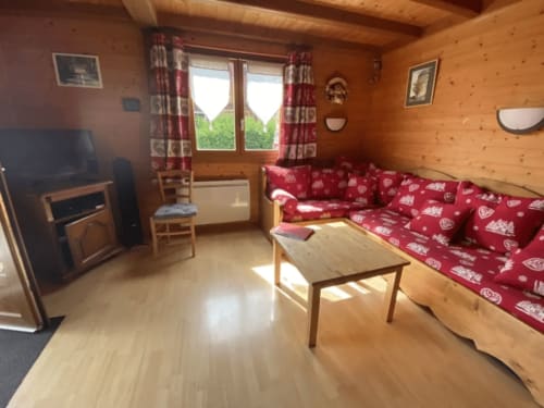 Séjour cozy de chalet en bois avec canapé fleuri rouge, TV et vues aux Gîtes Des Planchettes, Marigny