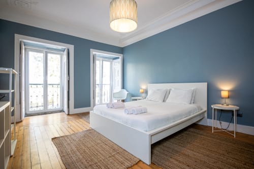 Suite moderna do VAGO Alcântara Suites, Lisboa, com paredes azuis, cama branca, soalho de madeira e portas de varanda