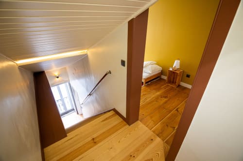 Corredor da Suite Tripla Duplex do VAGO Alcântara Suites, Lisboa, com piso de madeira, parede de destaque amarela e acesso aos quartos