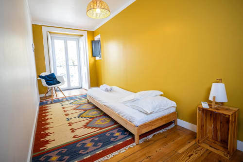 Quarto amarelo vibrante na VAGO Alcântara Suites, Lisboa com cama de madeira, tapete colorido e acesso à varanda