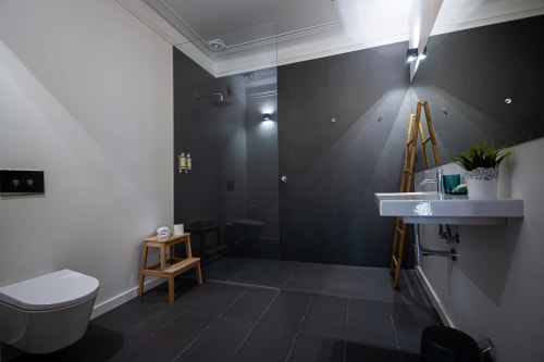 Banheiro moderno da VAGO Alcântara Suites, Lisboa, com azulejos pretos, pia flutuante, duche aberto e sanita branca.