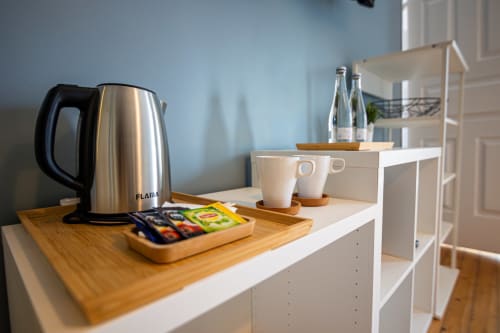 Kitchenette moderna da suíte do hotel com chaleira em aço inoxidável, canecas brancas e garrafas de água no VAGO Alcântara Suites em Lisboa