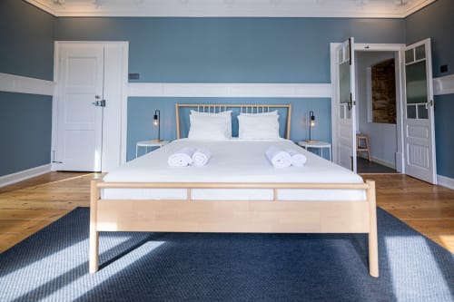 Suíte luminosa no VAGO Alcântara Suites, Lisboa com cama de madeira, paredes azuis, roupa branca e piso de madeira