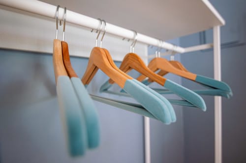 Quatro cabideiros de madeira e turquesa em trilho branco no quarto do hotel VAGO Alcântara Suites em Lisboa
