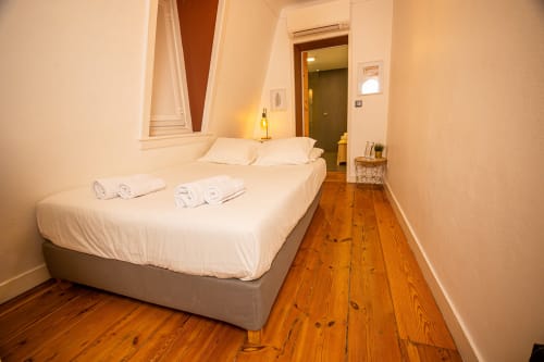 Acolhedor quarto de casal no VAGO Alcântara Suites em Lisboa com roupa de cama branca, piso em madeira e comodidades modernas