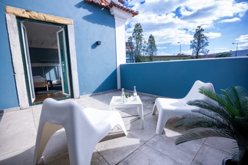 Terraço moderno das VAGO Alcântara Suites em Lisboa com espreguiçadeiras brancas, paredes azuis e vista para a cidade