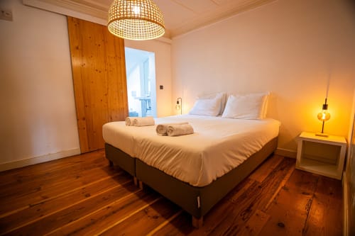 Quarto suíte moderno no VAGO Alcântara Suites em Lisboa com piso de madeira, cama queen, luminária de teto trançada e ambiente aconchegante