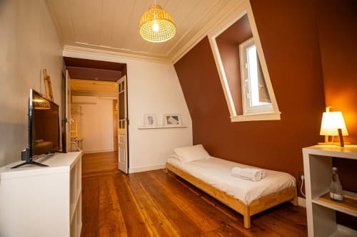 Espaçoso quarto do hotel VAGO Alcântara Suites em Lisboa com cama de madeira, paredes castanhas quentes, iluminação pendente e design moderno