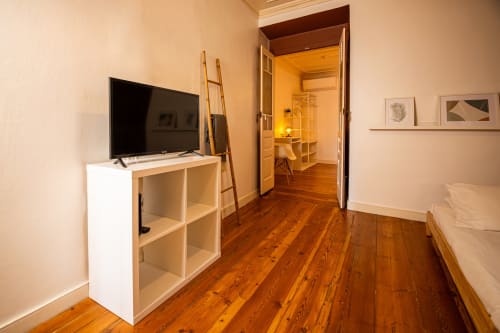 Entrada da suíte do hotel VAGO Alcântara Suites em Lisboa, com piso de madeira, TV em estante e acesso ao quarto