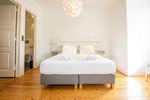 Quarto moderno da VAGO Alcântara Suites em Lisboa com piso de madeira, cama contemporânea e decoração minimalista branca