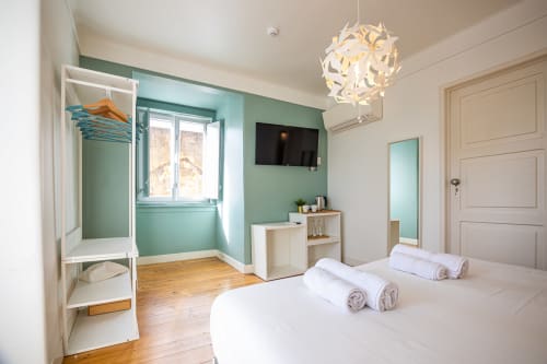 Suíte moderna do VAGO Alcântara Lisboa com cama, parede de destaque turquesa, TV, piso em madeira e luminária pendente