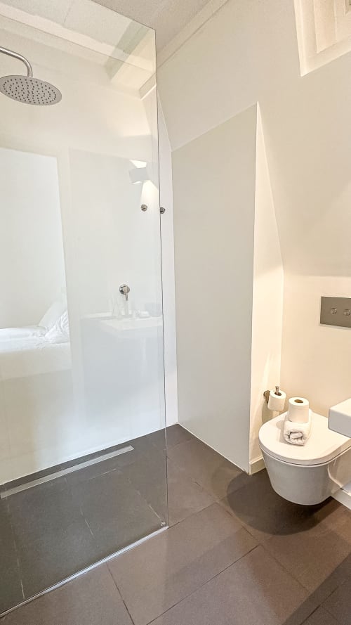 Banheiro moderno na VAGO Alcântara Suites em Lisboa com chuveiro walk-in, sanita e produtos de higiene
