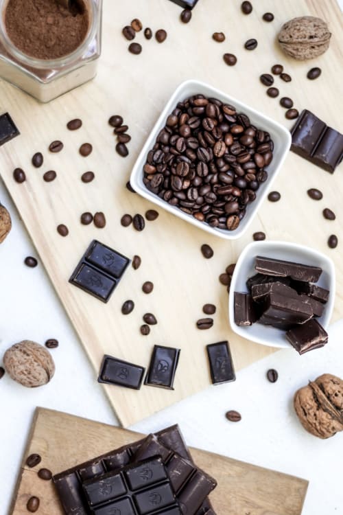 Grains de café, cacao en poudre, chocolat noir, fruits secs et biscuits disposés sur une surface en bois aux Gîtes Des Planchettes, Marigny