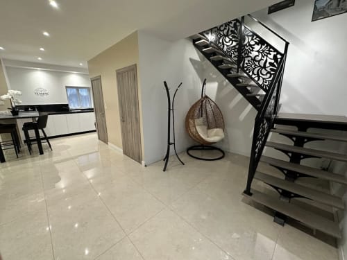 Hall d'entrée moderne aux Gites Les Camelias 71 avec chaise suspendue, escalier noir et carrelage blanc brillant