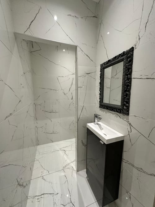 Salle de bain moderne aux Gites Les Camelias 71 à Oslon : murs en marbre, miroir à cadre noir et vasque blanche épurée