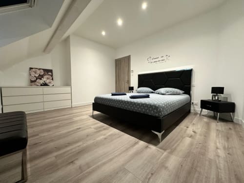 Chambre moderne aux Gites Les Camelias 71 avec lit noir, mobilier blanc, parquet et accès à la vue du jardin.