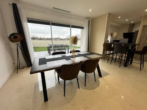 Salle à manger moderne aux Gîtes Les Camelias 71 avec table noire, chaises marron et grandes fenêtres sur la campagne d'Oslon