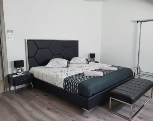 Chambre moderne aux Gîtes Les Camelias 71 à Oslon avec lit à tête de lit hexagonale noire, literie à motifs, table de nuit et banc