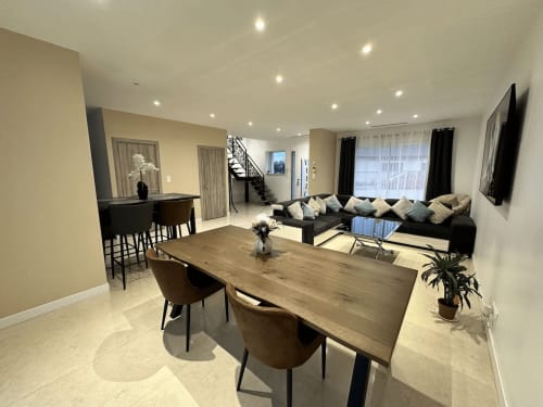 Séjour ouvert et moderne aux Gîtes Les Camélias 71 avec table à manger, canapé noir et escalier